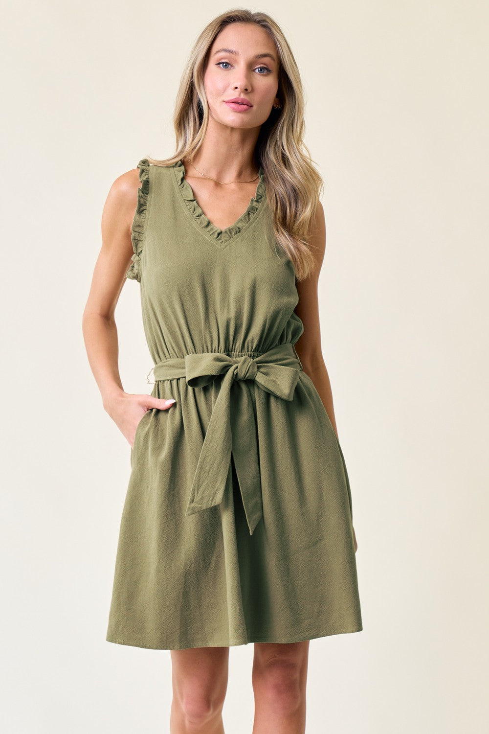 A woman wearing a Doe and Rae 27476D Short Sleeveless V Neck Tie Front Dress with a ruffled belt.